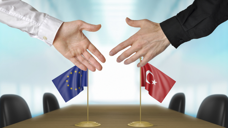 Two diplomats from the European Union and Turkey extending their hands for a handshake on an agreement between the countries.