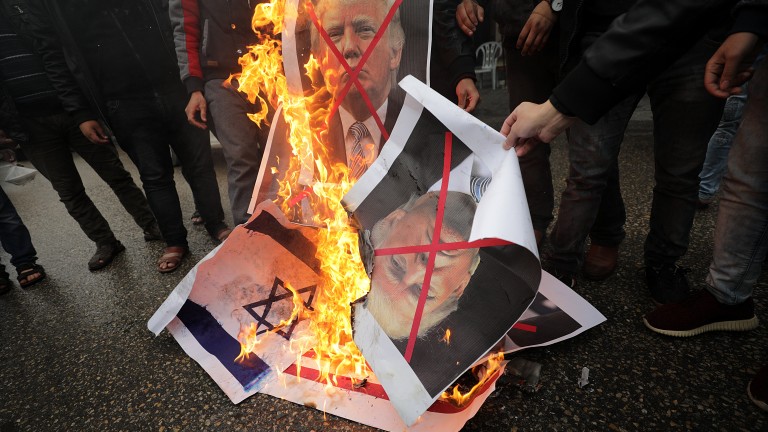 epa06371733 Palestinians burn Israeli and US flags and posters of US President Donald Trump and Israeli Prime Minister Benjamin Netanyahu during protest against the US intention to move its embassy to Jerusalem and to recognize the city of Jerusalem as the capital of Israel, in Rafah, southern Gaza Strip, 06 December 2017. According to media reports, US President Donald J. Trump has informed Palestinian leader Mahmoud Abbas that he intends to recognize Jerusalem as the Israeli capital and will relocate the US embassy from Tel Aviv to Jerusalem.  EPA/MOHAMMED SABER