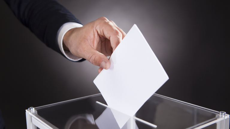 Cropped image of businessman inserting ballot in box on desk against black background
