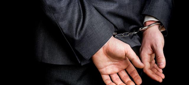 Arrested businessman in handcuffs with hands behind back - isolated on black background